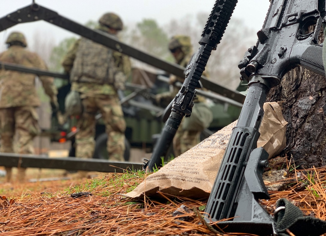 Weapons are placed against trees while U.S. Army Soldiers build a tent during an area defense field training exercise at Joint Base Langley-Eustis, Virginia, Feb. 13, 2020.