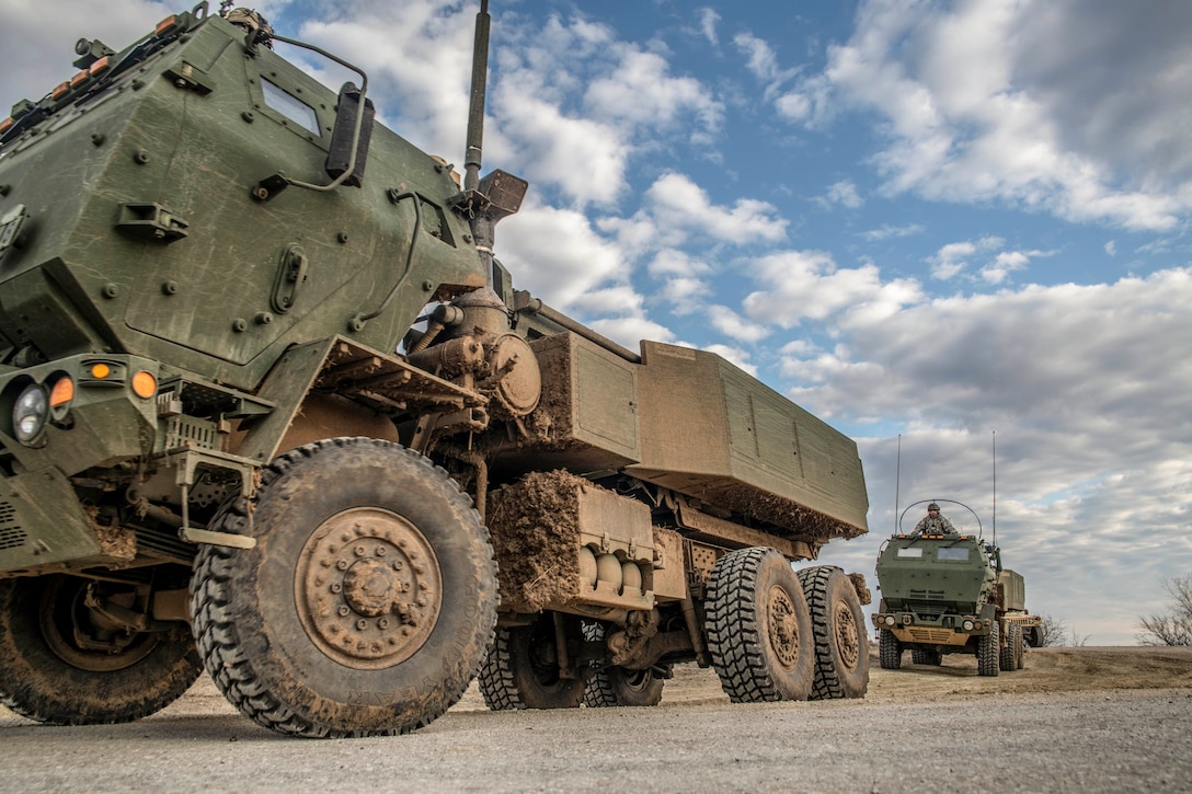 Army vehicles travel on a road.