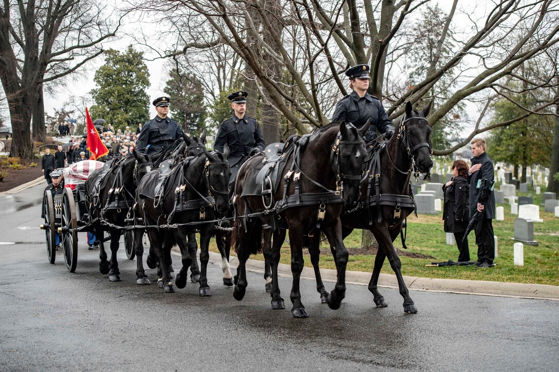 A procession led by troops on horseback advances forward on a cemetery road.