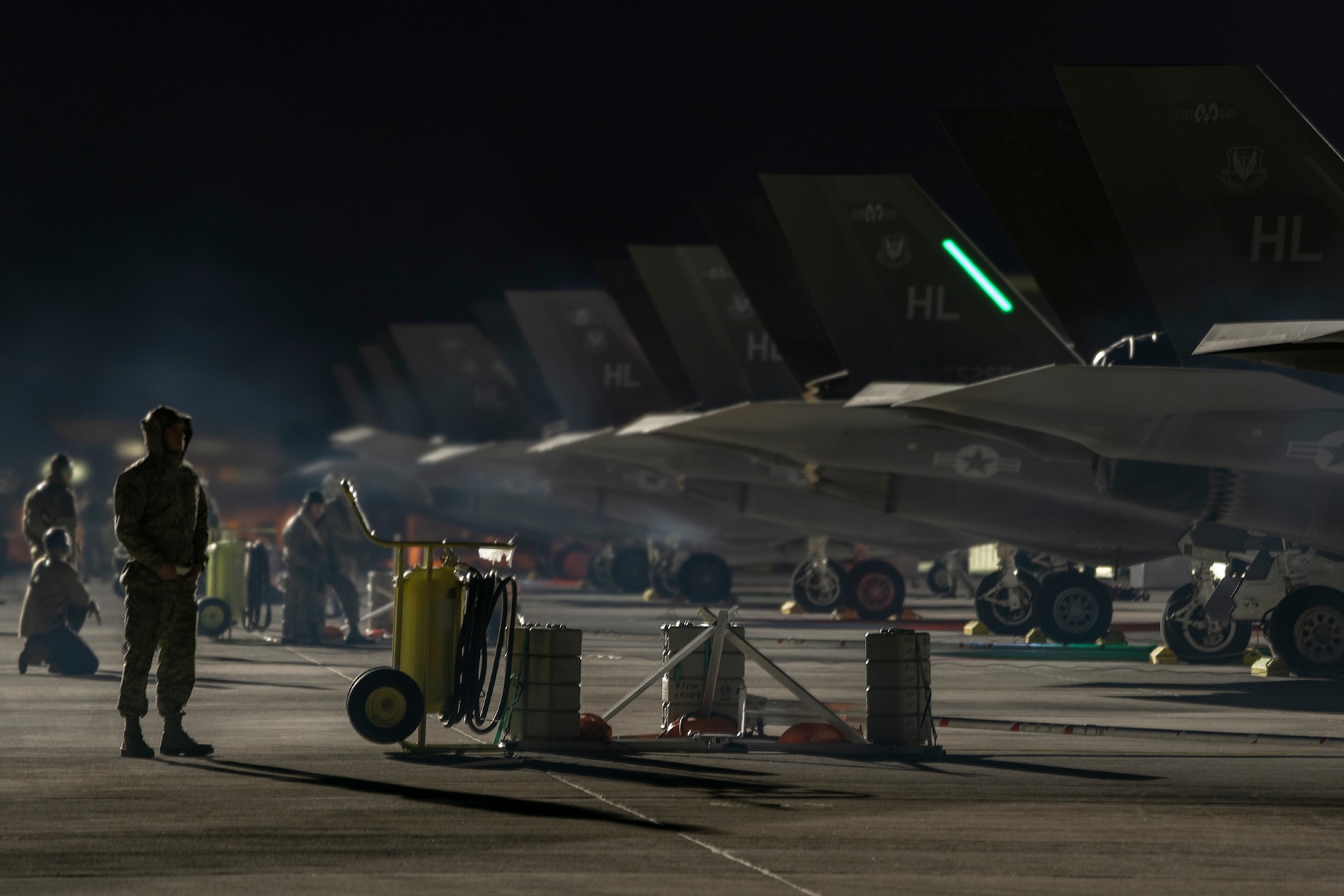 Airmen stand behind a row of F-35A Lightning II fighter jets at night.