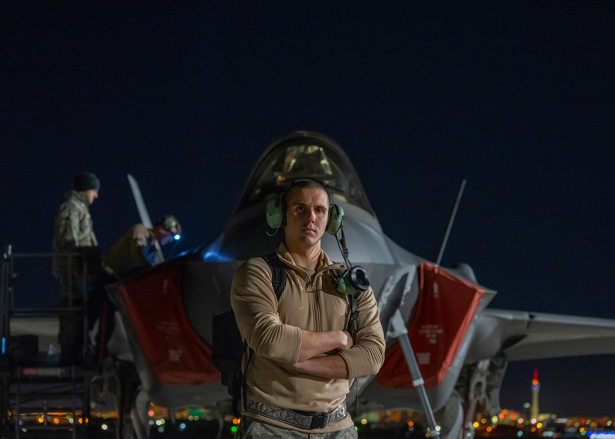 An Airman stands in front of an F-35A Lightning II fighter jet at night.