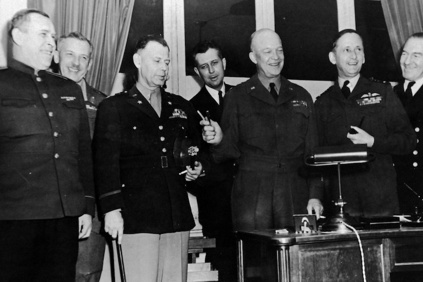 A group of military officials stand together with one of them holding a pen.