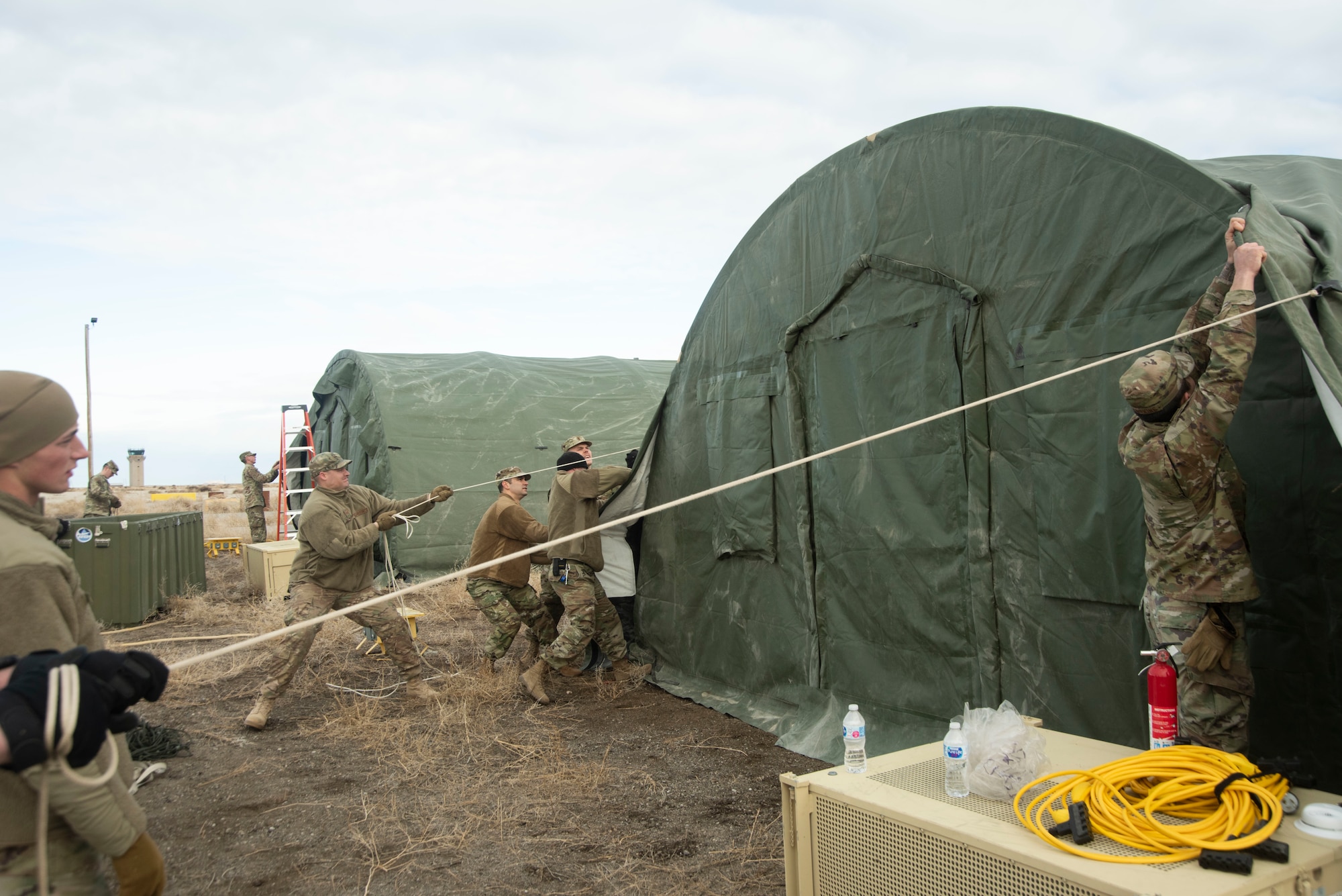 A group of U.S. Air Force Airmen secure a tent cover, Jan. 23, 2020, on Mountain Home Air Force Base, Idaho. This training was conducted to equip Airmen with skills from other career fields to enhance their readiness and multi-functionality. (U.S. Air Force photo by Airman 1st Class Akeem K. Campbell)