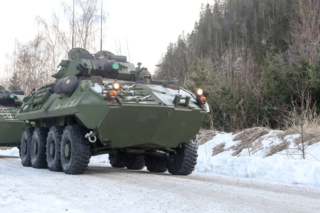 A military vehicle heads down a snow-covered road.