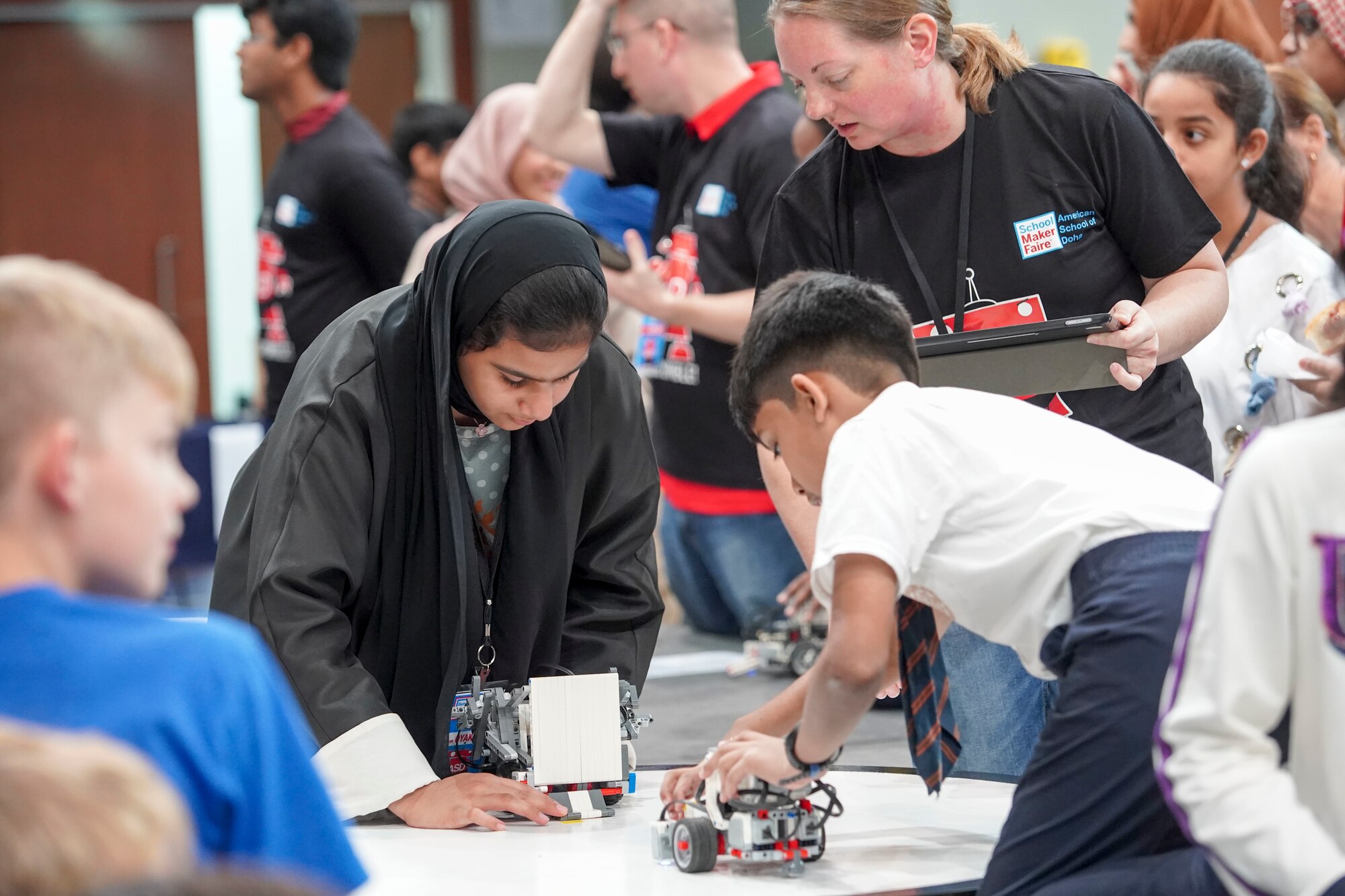 Airmen with 379th Expeditionary Civil Engineering Squadron explosive ordnance disposal team teach students how to operate a bomb defusal robot at American School of Doha’s Maker Faire in Doha, Qatar, on Jan. 25, 2020. EOD Airmen volunteers gave students attending the faire a hands-on experience driving the robots through an obstacle course where they were tasked with using a robot to grab a cone and stack it on another cone. (Courtesy Photo)