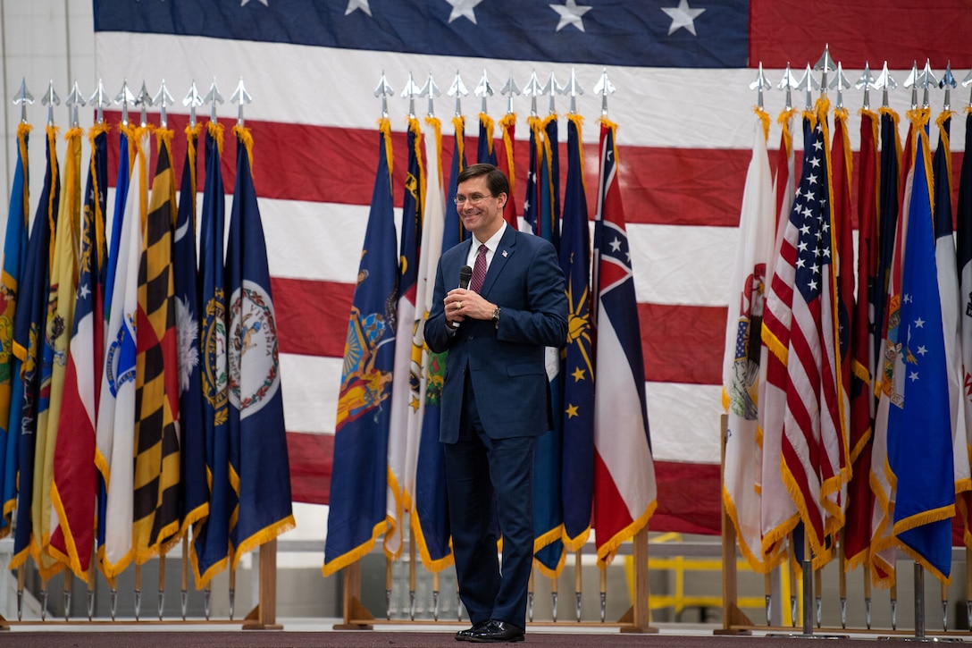 Defense Secretary Dr. Mark T. Esper speaks on a stage with flags behind him.