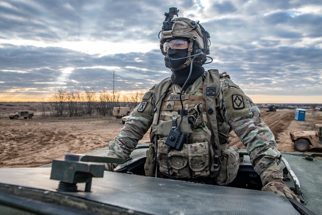 A soldier looks out of the top of a vehicle in the desert.