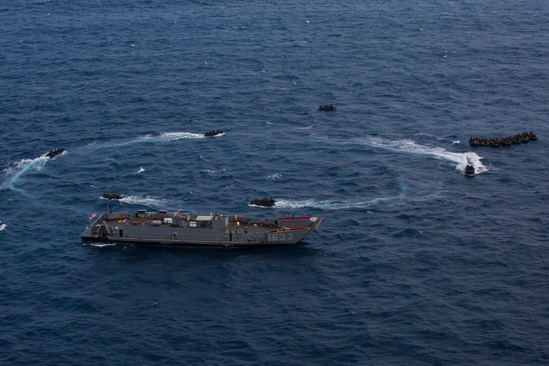 A group of combat rubber raiding crafts and other vessels travel through waters in a circle.