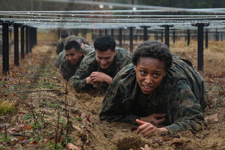 A line of Marines crawl underneath barbed wire.