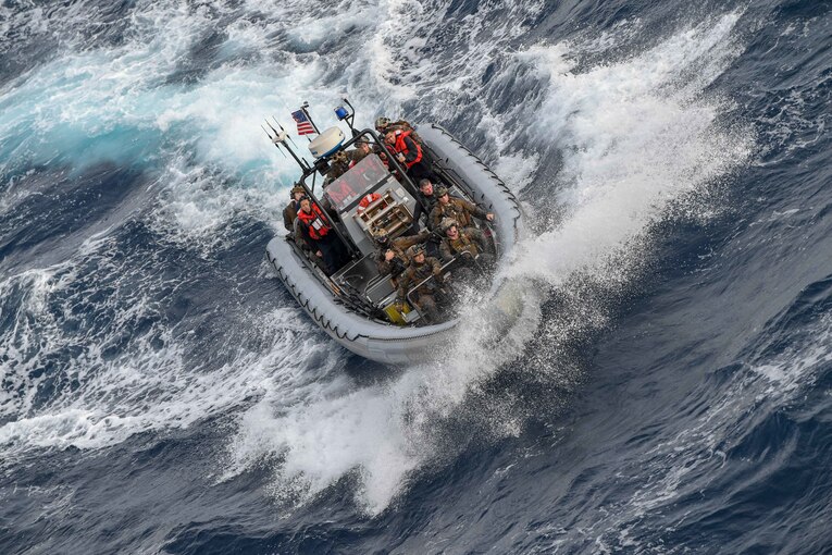 A group of sailors and Marines ride in an inflatable boat.