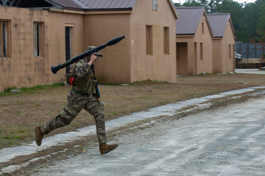 A Marine runs across a street carrying a simulated weapon.