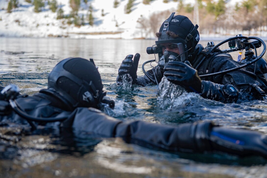 Two sailors move in water up to their shoulders.