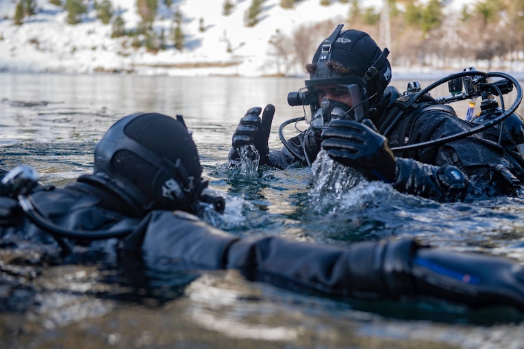 Two sailors move in water up to their shoulders.