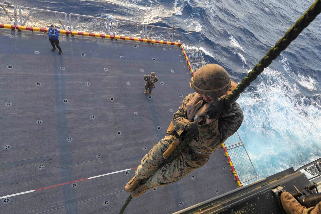 A Marine slides down a rope onto the deck of a ship.