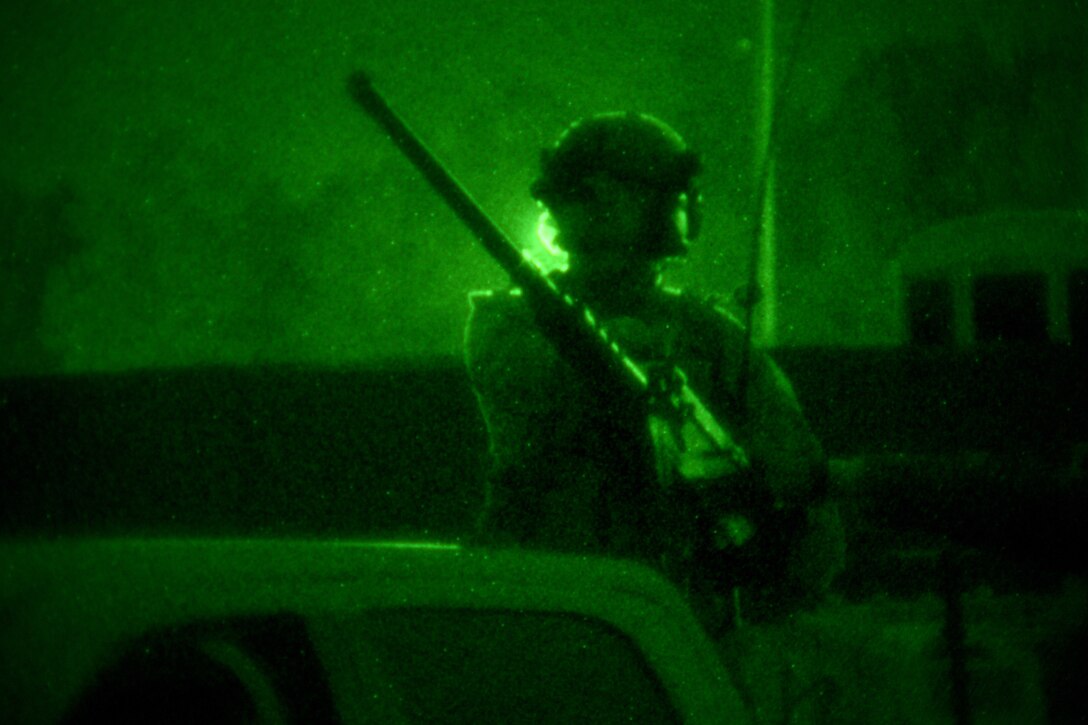 An airman holds a weapon illuminated by a green light.