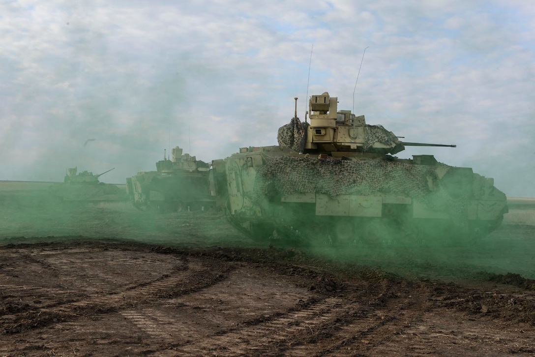 Tanks move through a dirt road surrounded by green smoke.