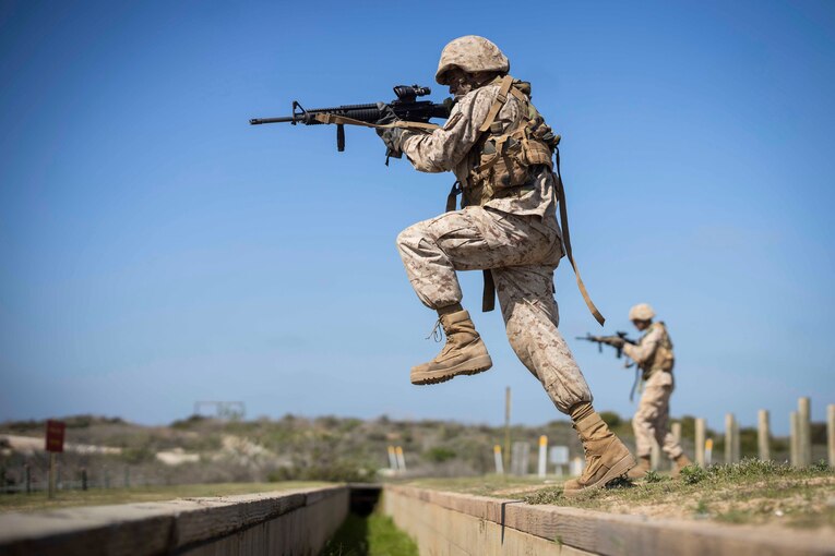 A Marine Corps recruit holds up a weapon while in midstep.