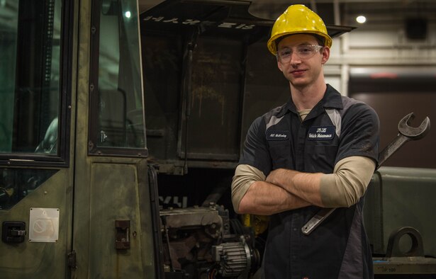 Vehicle maintainer poses in front of forklift.