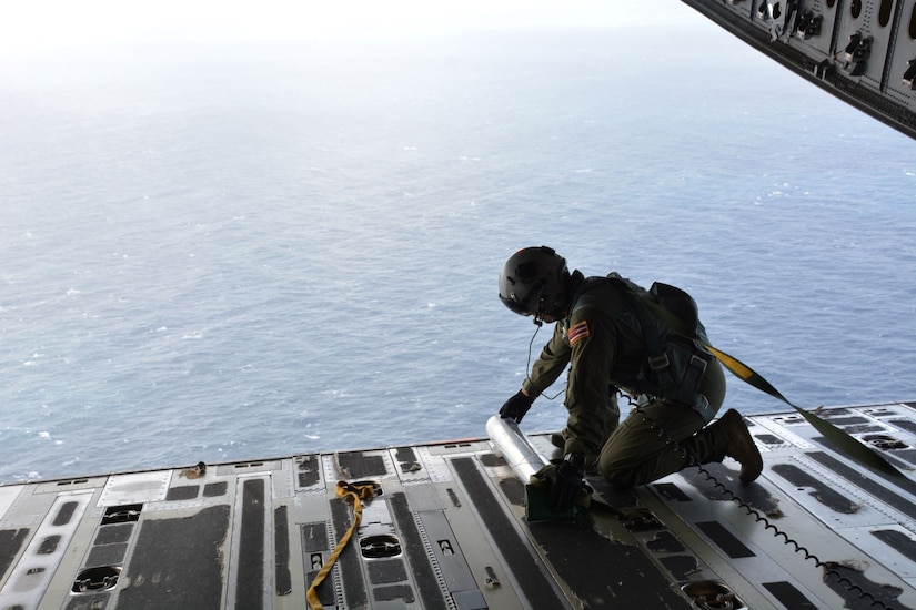 A service member crouches on the ramp of a C-17 aircraft.