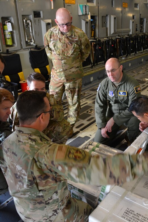 Three Airmen talk onboard a C-17 aircraft.