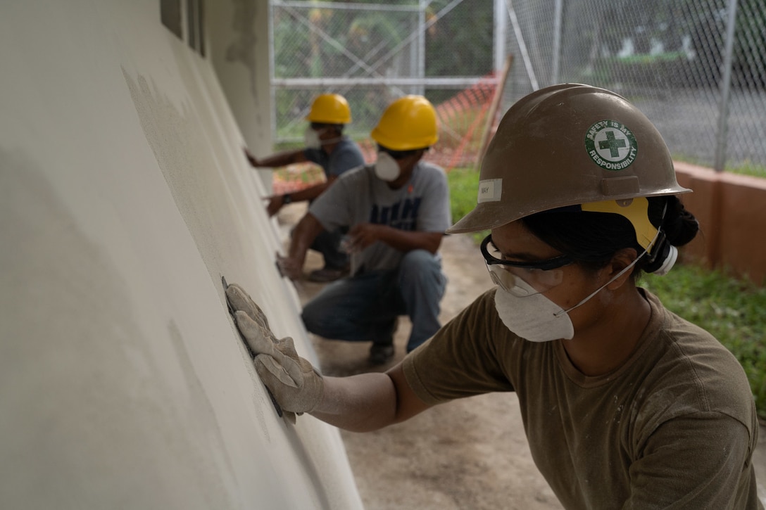 A sailor wearing a mask and helmet wipes a wall, as civilians in the background the same.