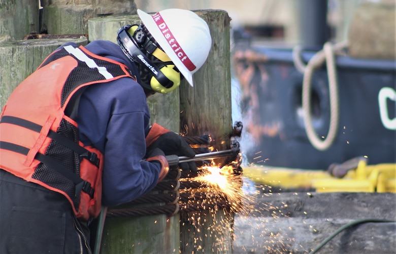 A man in a hardhat uses a torch to deconstruct wooden pilings in Rudee Inlet