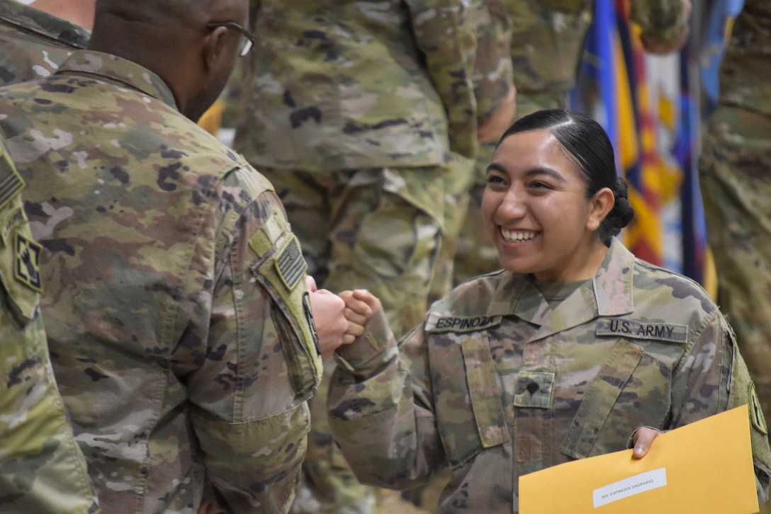 A smiling soldier fist-bumps another.