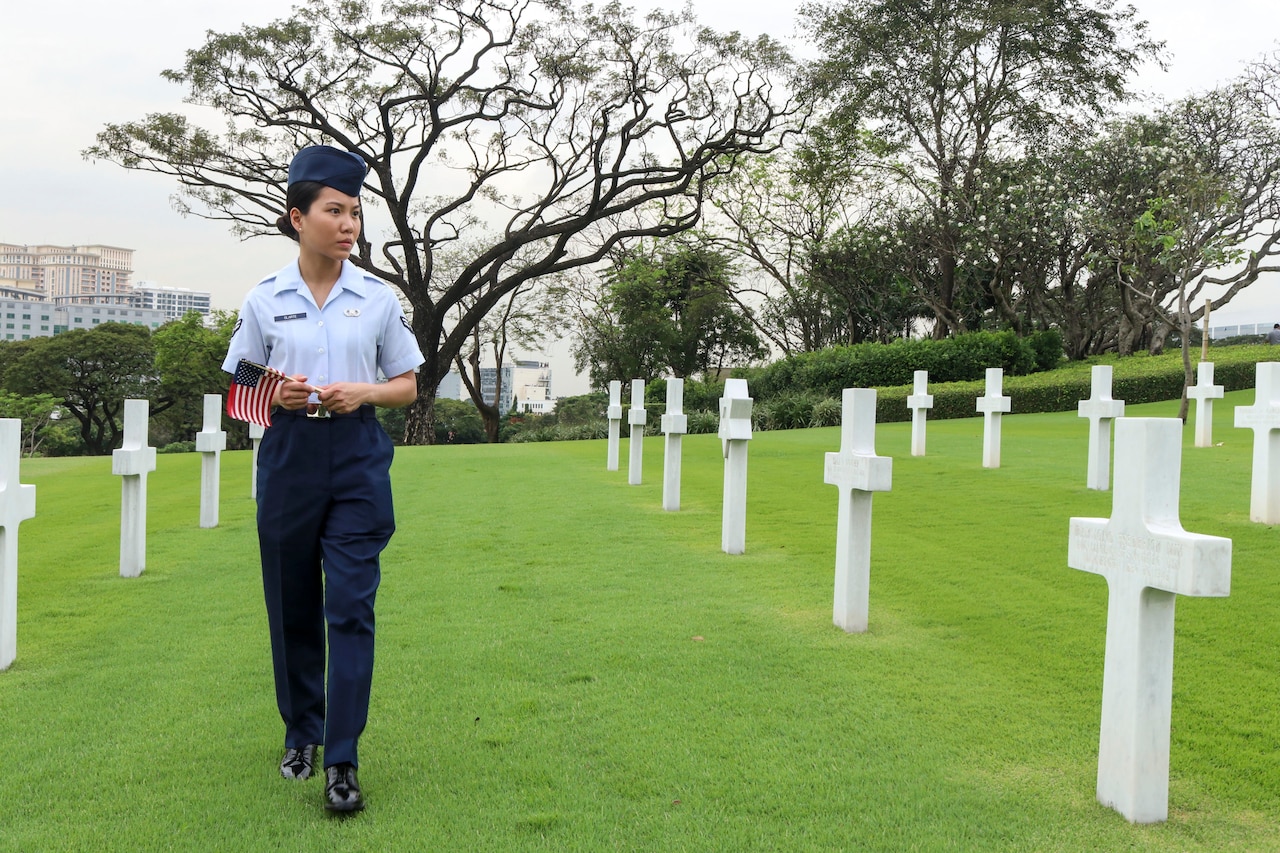 An airman walks past gravestones holding a small American flag.