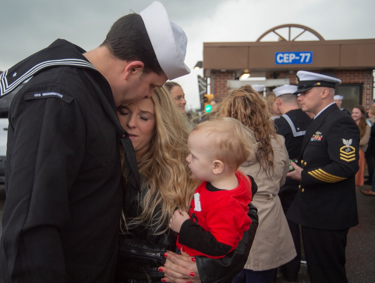 A service member hugs a woman and child.