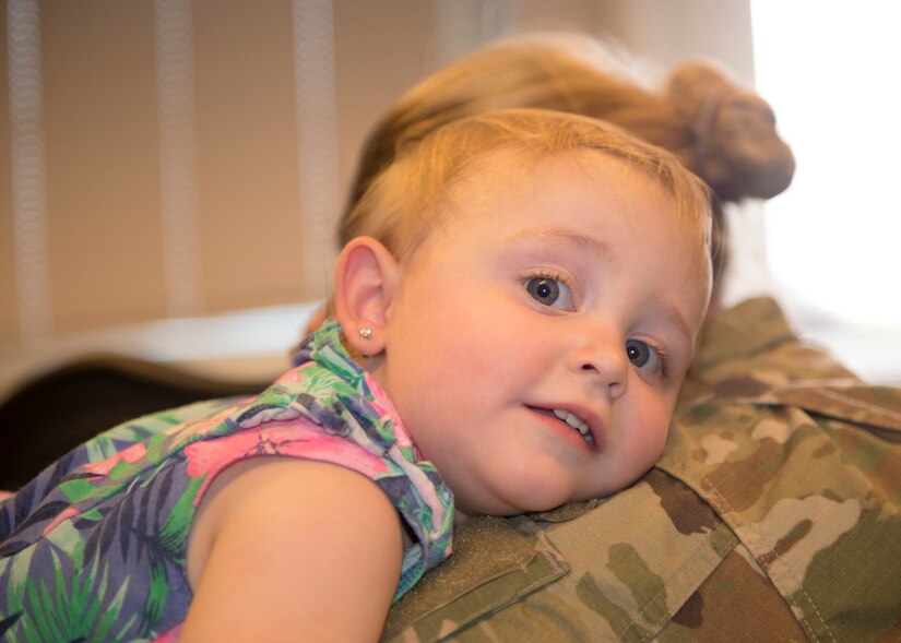 A small child rests her head on a service member’s shoulder.