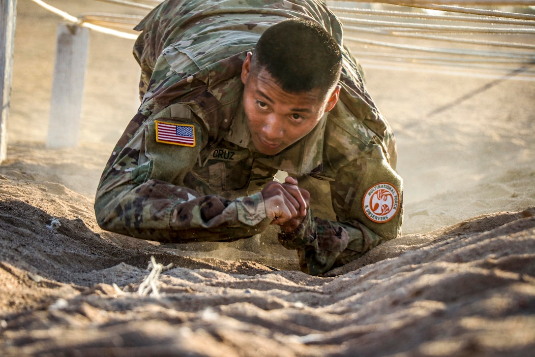 A soldier is crawling under ropes.