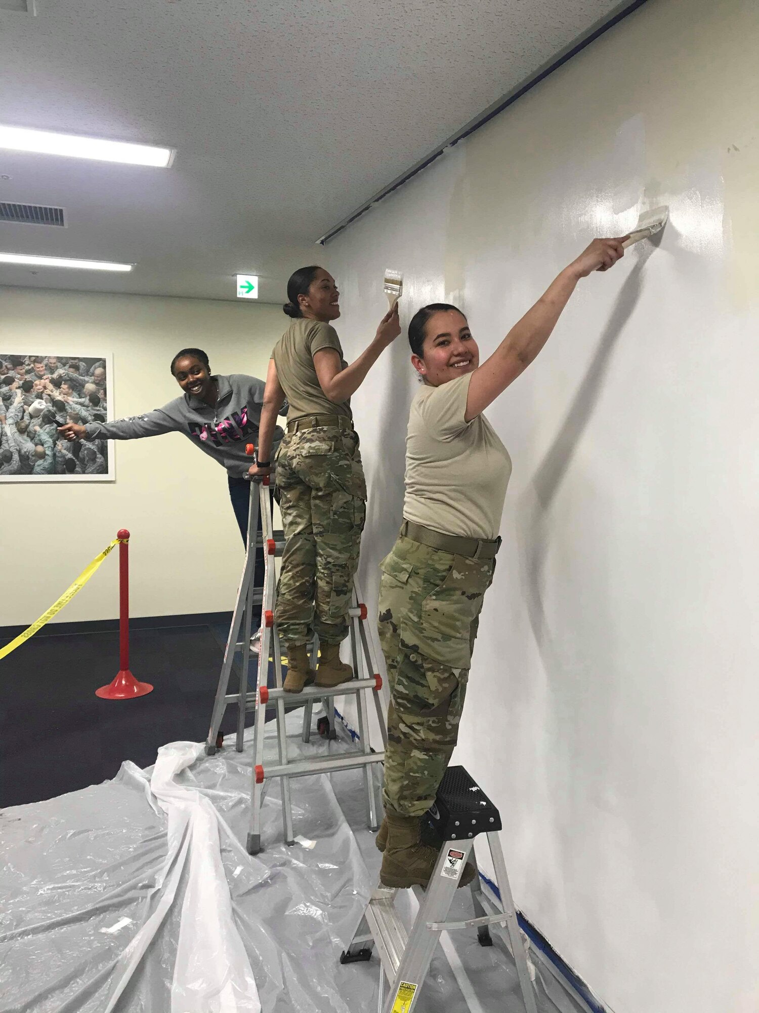 (From right) Senior Airman Karen Villalobos, 374th Security Forces Squadron pass and registration clerk, Tech. Sgt. Latisha Langley, 374 SFS NCO in charge of pass and registration office, and Airman 1st Class Te’Anne Dailey, 374 SFS patrolman, apply primer to a wall before painting a mural at Yokota Air Base, Japan, Jan. 31, 2020.