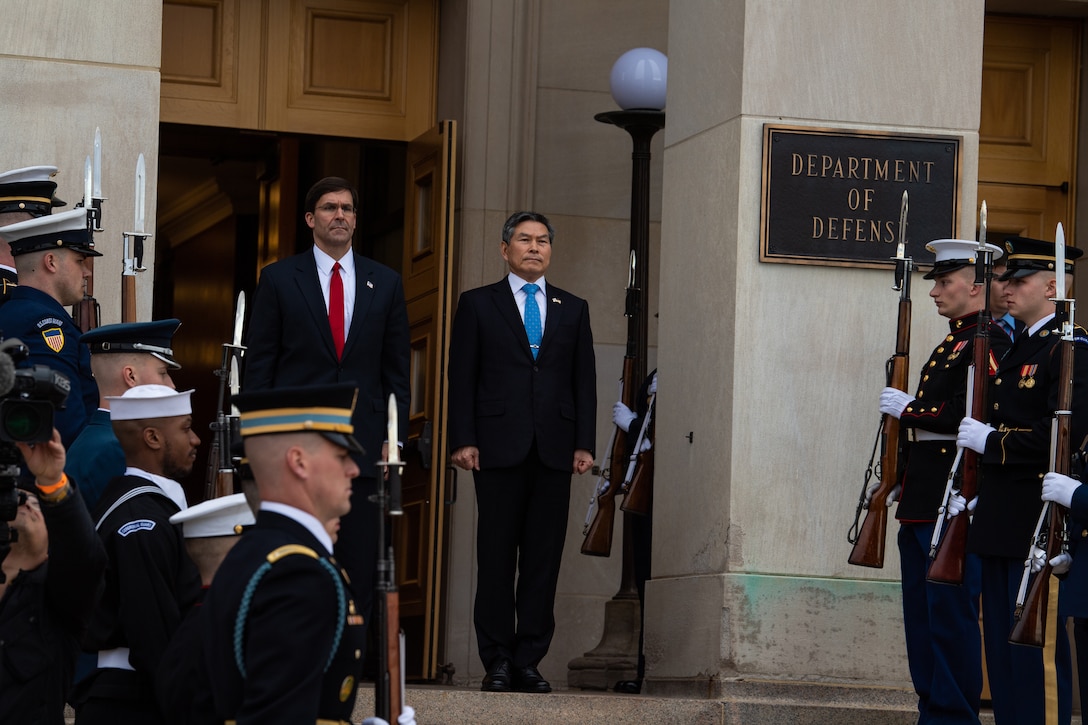 Two men stand at the top of some stairs with service members on each side of them.