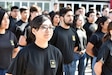 woman wearing black army shirt stands in line with other young people.