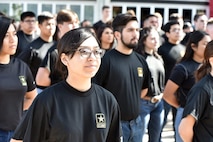 woman wearing black army shirt stands in line with other young people.