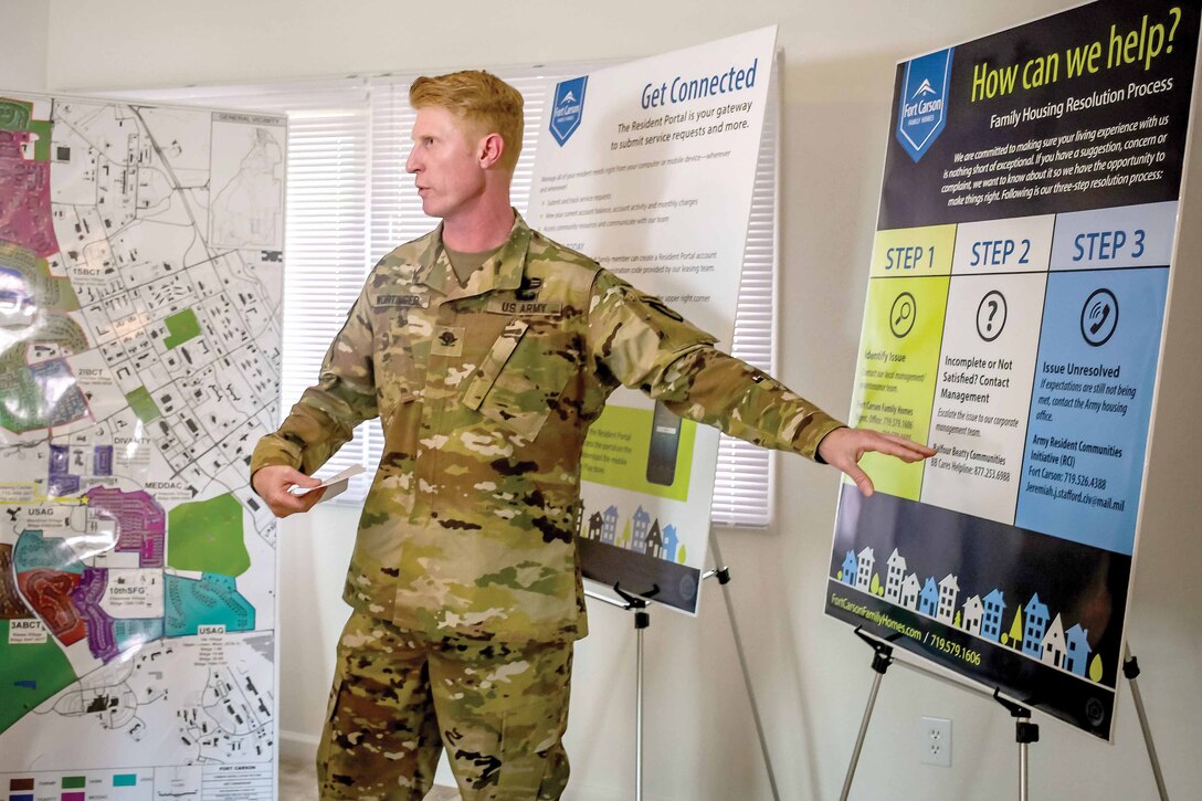 A military officer points at a slide projected behind him.