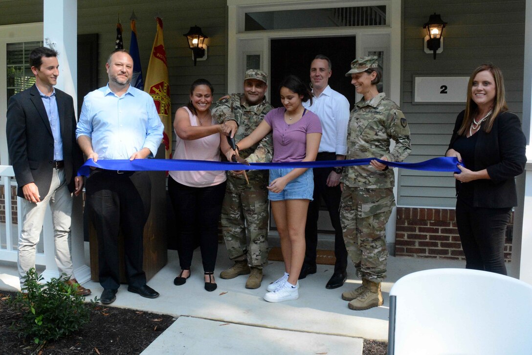 Civilians and service members cut a blue ribbon while standing on the porch of a home.