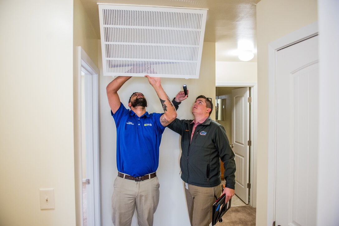 Two men inspect a ceiling vent in a home.