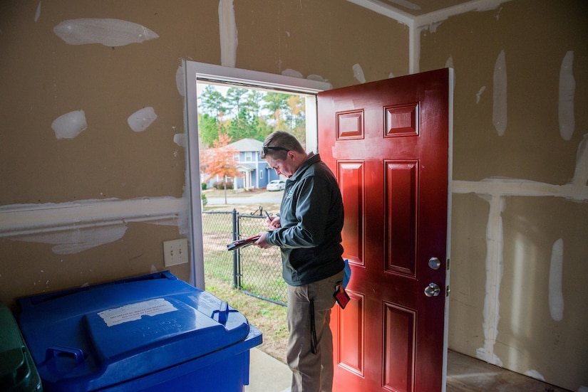 A man makes notes on a clipboard while standing in a doorway.