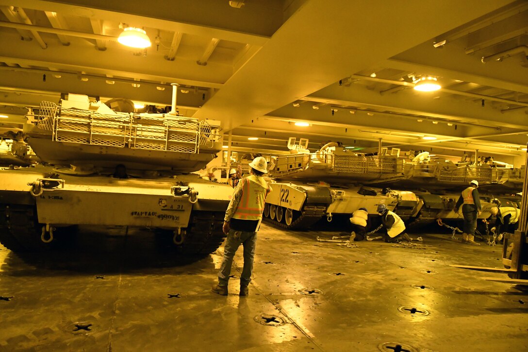 Workers secure tanks in hold of ship.