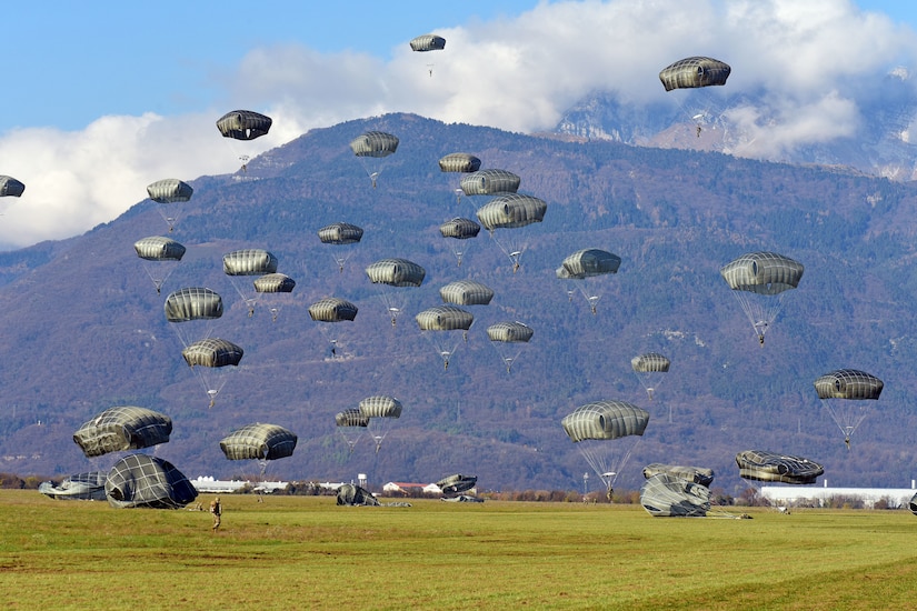 Nearly 25 paratroopers descend onto a grassy plain.