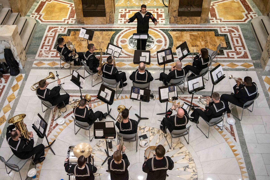 A group of sailors sit on chairs while playing different instruments.