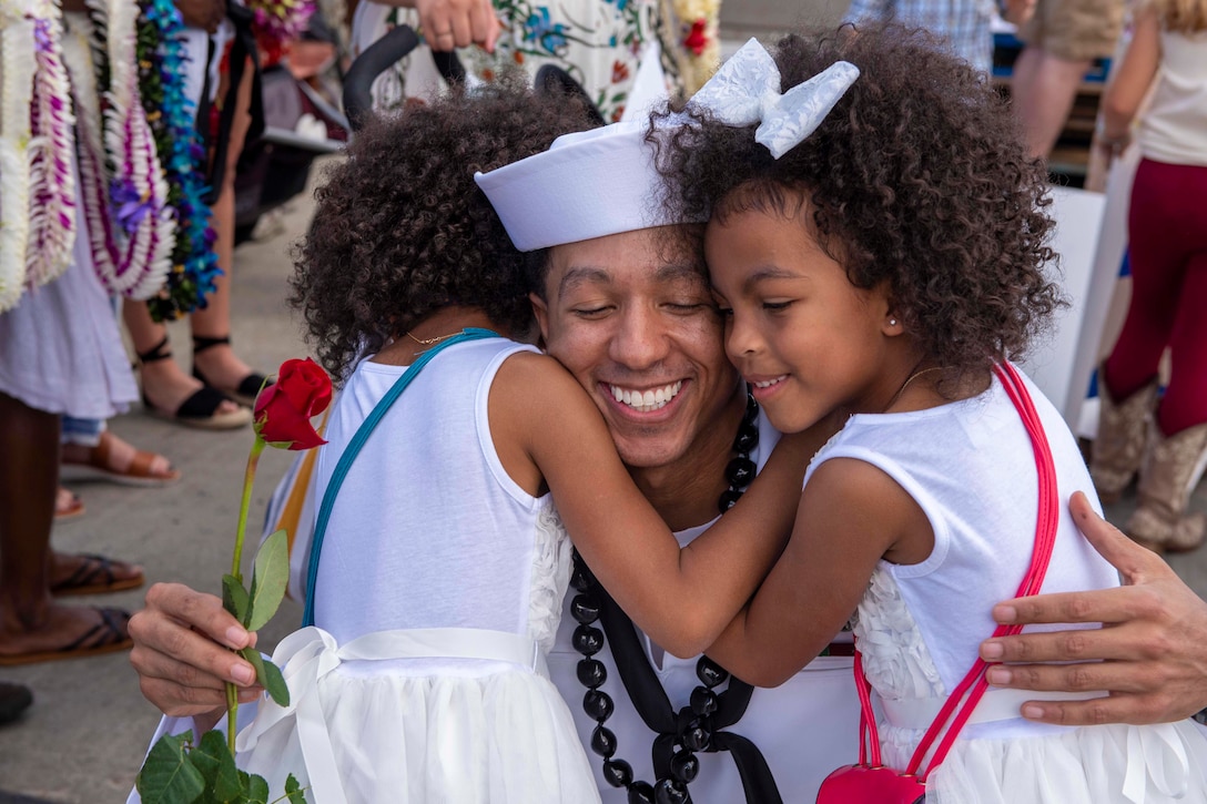 A sailor hugs two children.