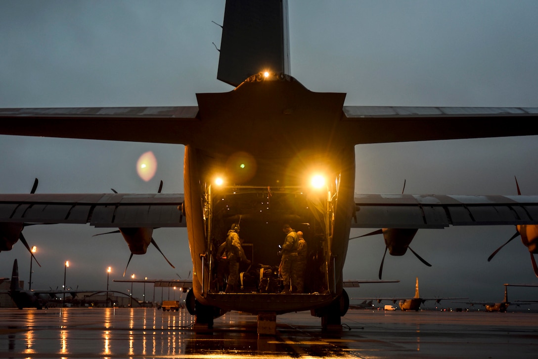 Airmen stand in an aircraft parked on a runway.