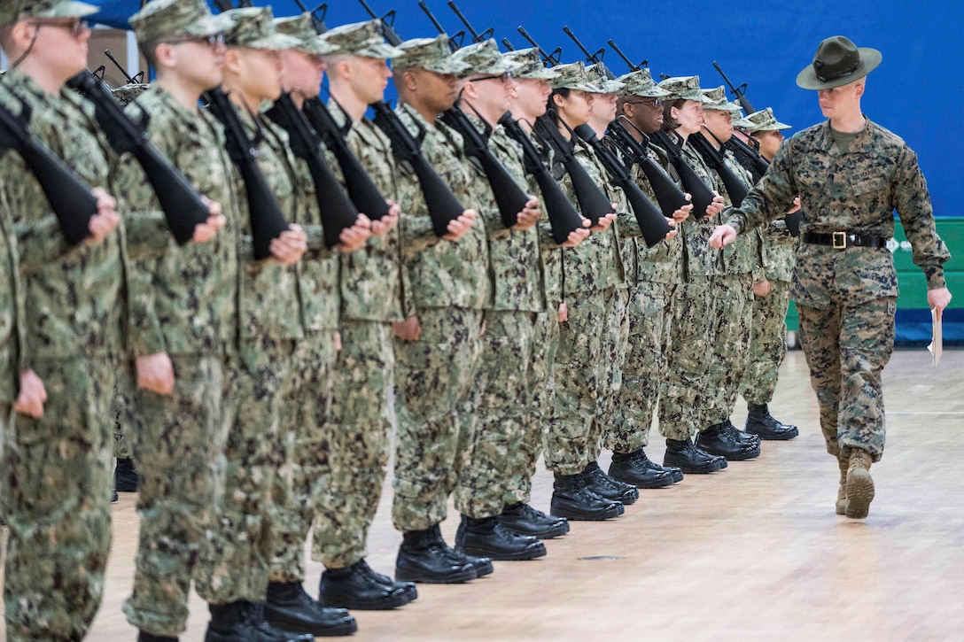 A Marine watches service members standing in as straight line.