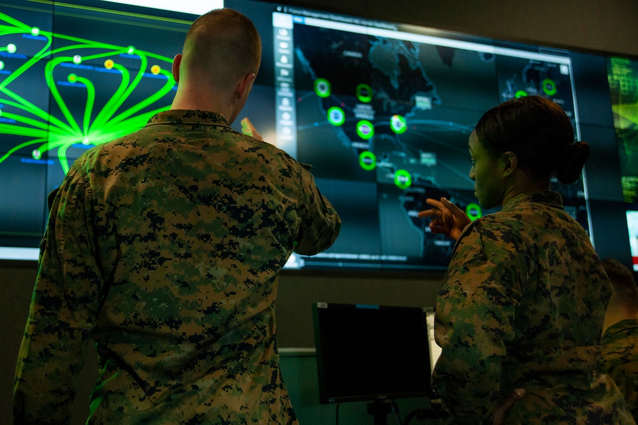 Two people look at wall-mounted computer screens.