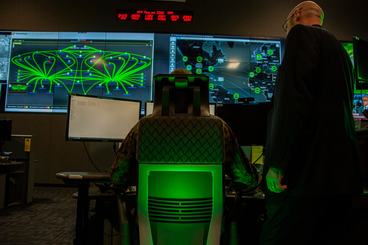 Two people look at wall-mounted computer screens.