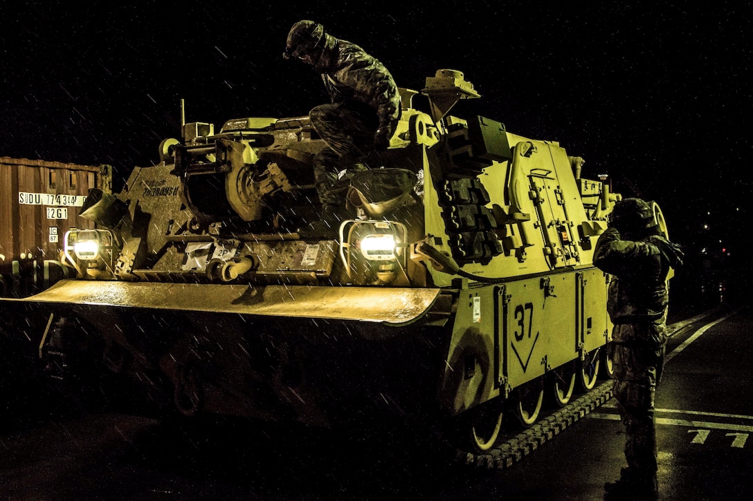 Soldiers and civilians inspect a tank in the dark.