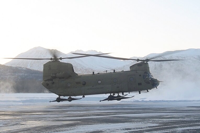An aircraft takes flight on a snowy runway in front of mountains.
