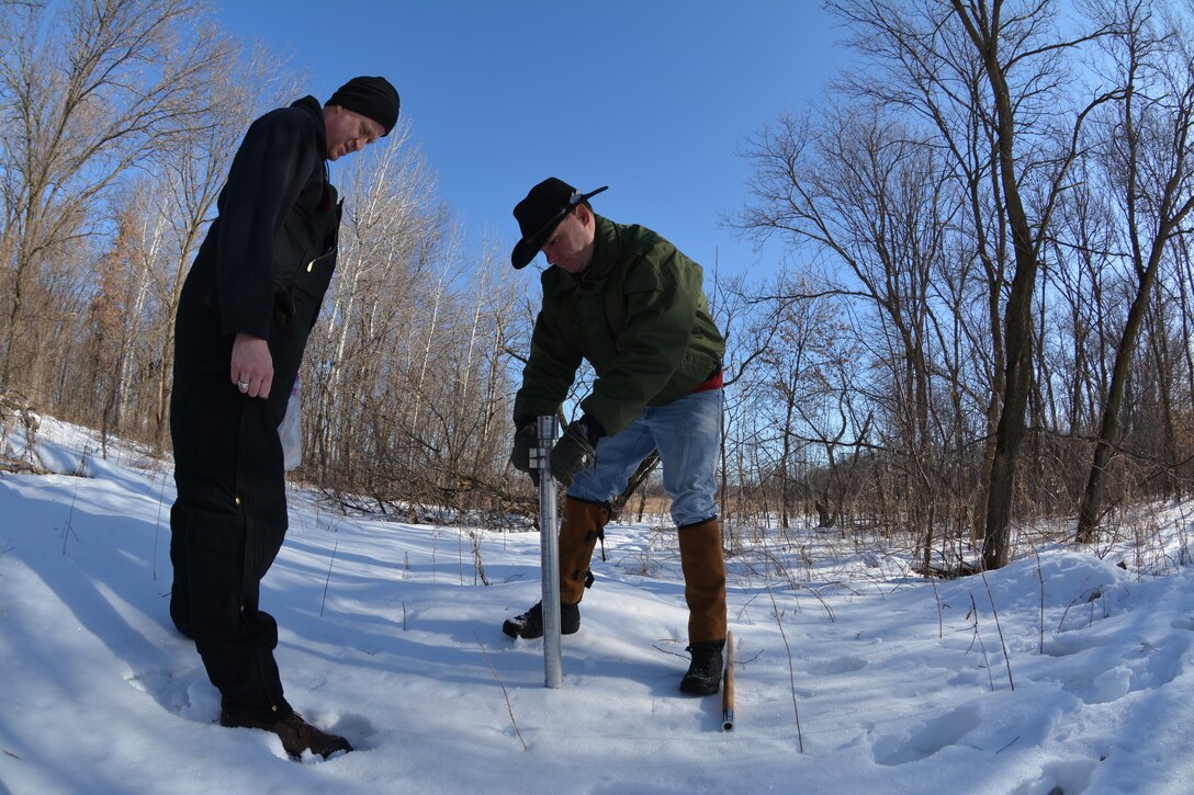 Two men take a snow sample with a snow tube